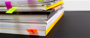 A stack of bound reports with stickers coming out of the book. Photo by Bernd Klutsch via Unsplash.